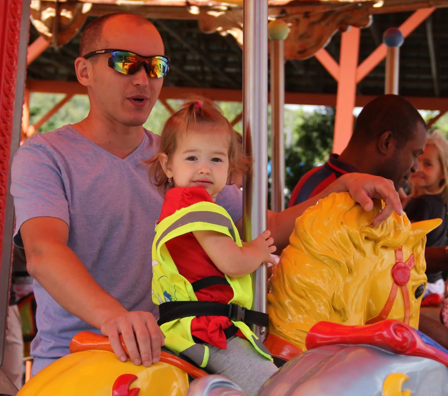 Tout-petit en dossard jaune sur un cheval de carrousel avec un adulte