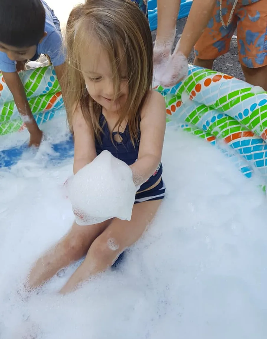 Fillette souriante tenant une poignée de mousse dans une piscine gonflable remplie de bulles