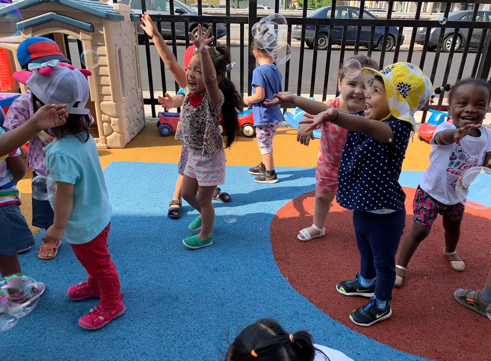 Enfants rieurs avec leurs chapeaux de soleil, les bras levés pour attraper de grosses bulles dehors