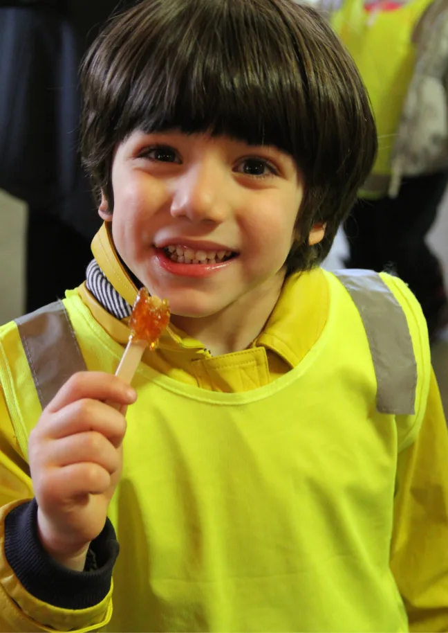 Un garçon souriant en dossard jaune déguste sa tire d'érable sur bâton