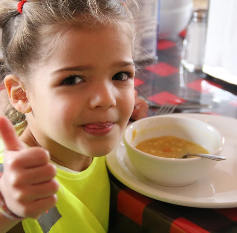 Une fillette souriante lève le pouce devant son bol de soupe