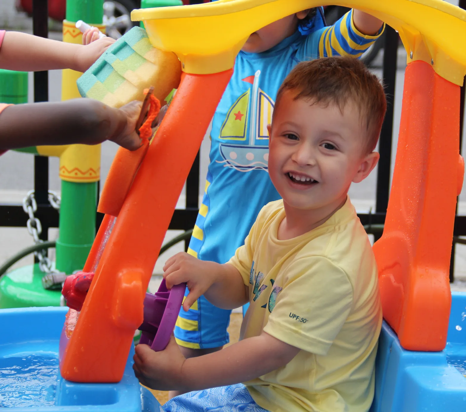 Petit garçon souriant en chandail jaune qui s'amuse à la table d'eau colorée avec ses amis