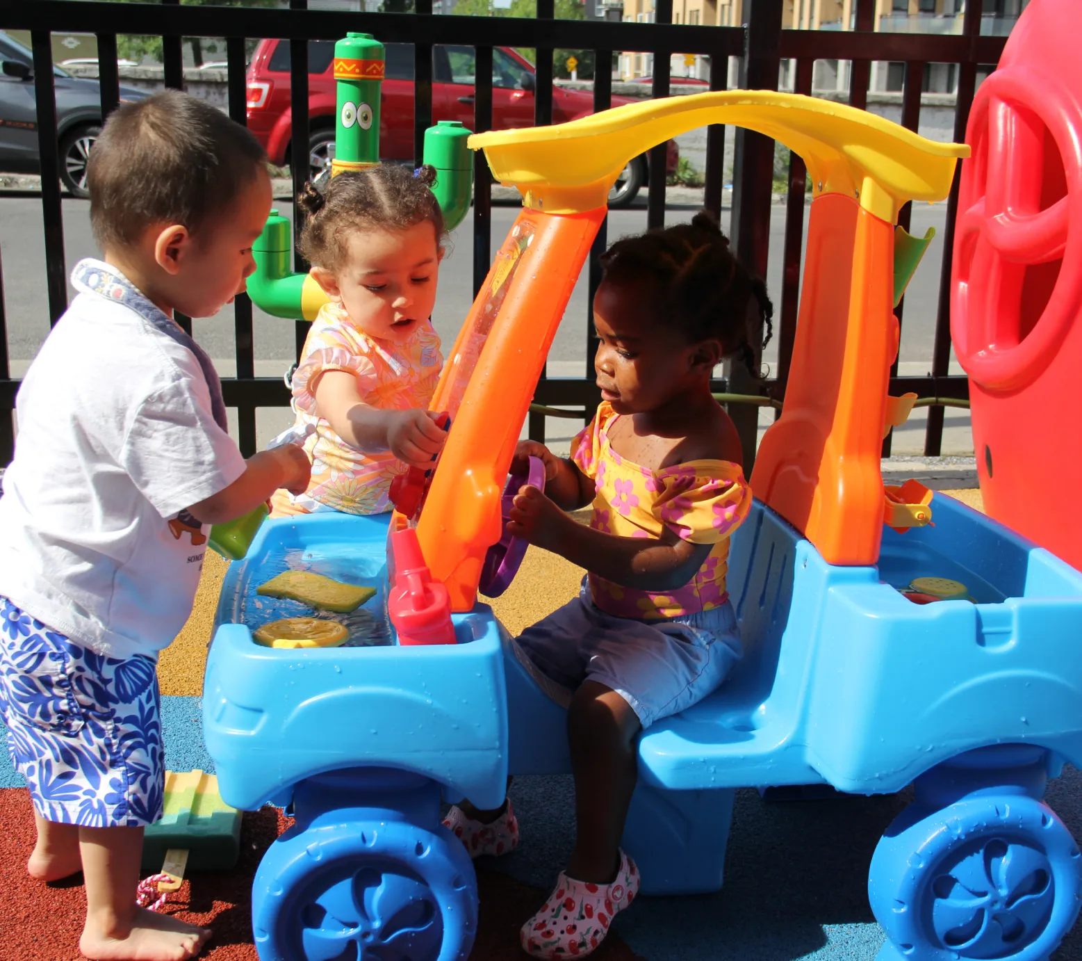 Trois tout-petits qui remplissent de jouets une petite auto bleue au lave-auto extérieur sous le soleil