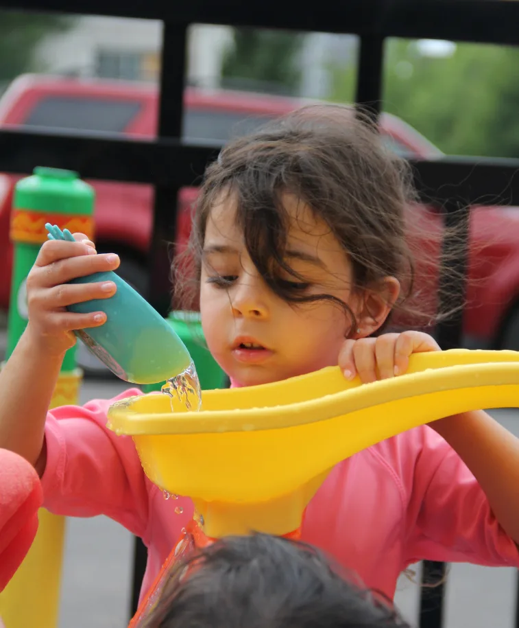 Petite fille concentrée qui presse une bouteille d'eau au-dessus d'un entonnoir jaune