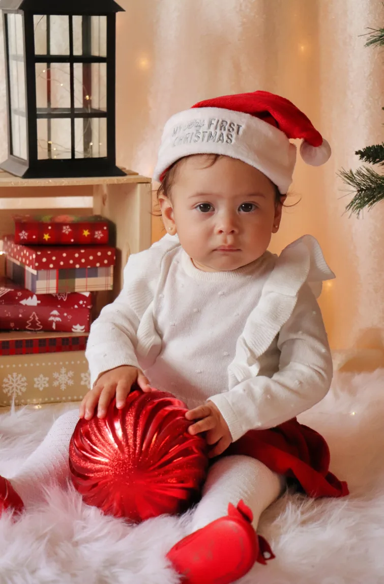 Bébé coiffé d'une tuque de père Noël qui tient une grosse boule rouge