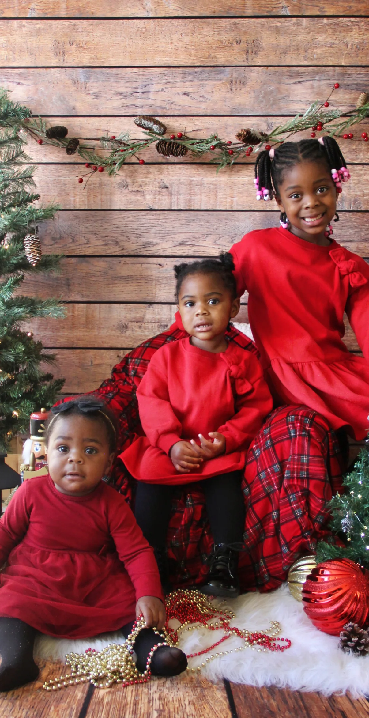 Trois fillettes en robes rouges assorties qui posent à côté d'un sapin décoré