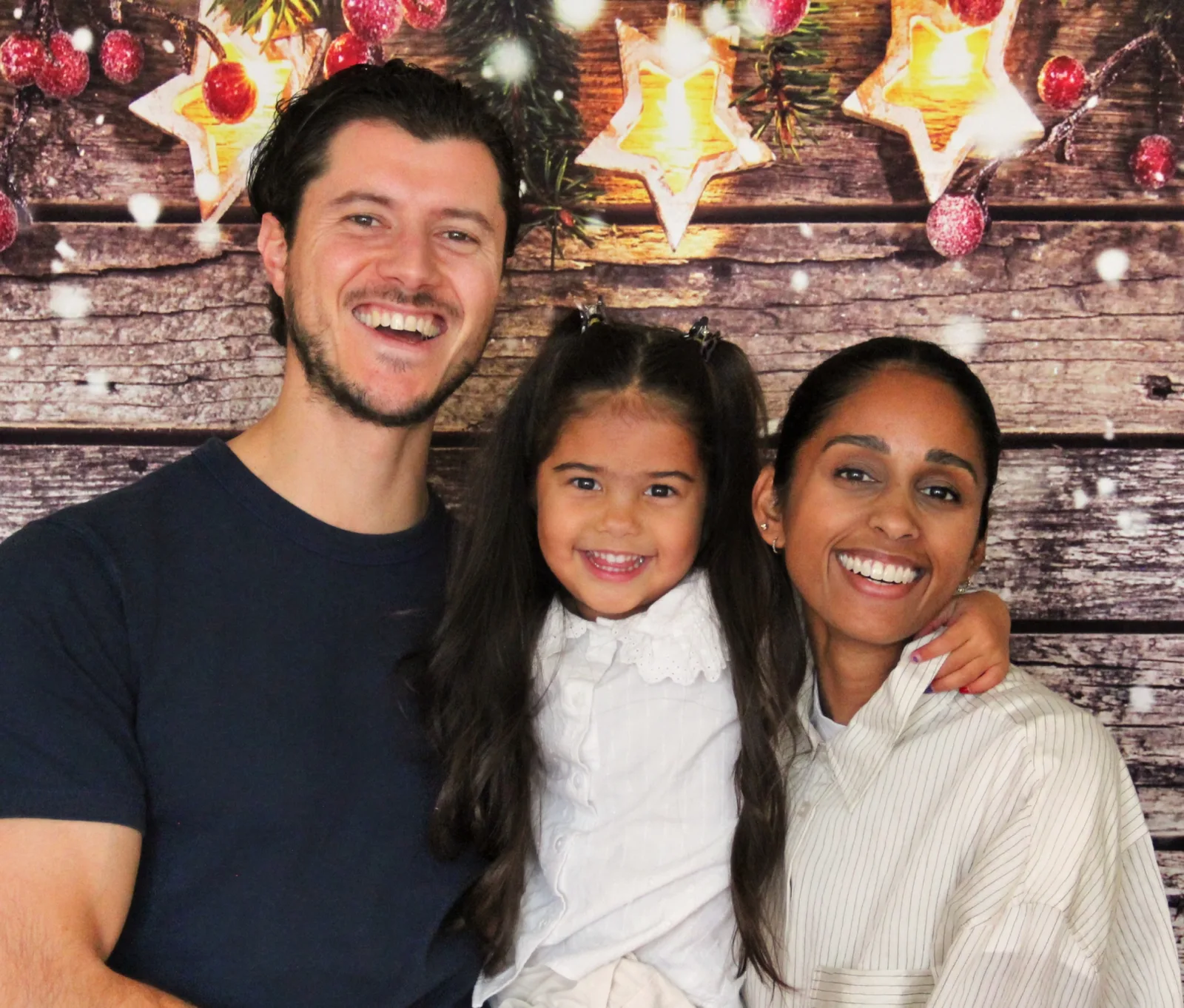 Parents souriants tenant leur petite fille devant un décor de bois orné d'étoiles lumineuses