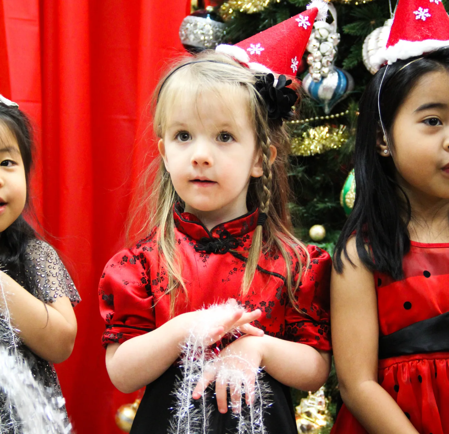 Trois fillettes en robes rouges des Fêtes tiennent des guirlandes près du sapin décoré