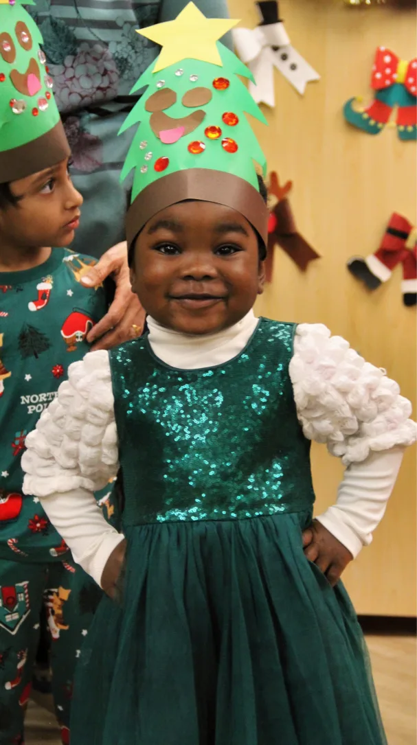 Bambine souriante en robe verte scintillante, coiffée d'un chapeau de sapin en papier