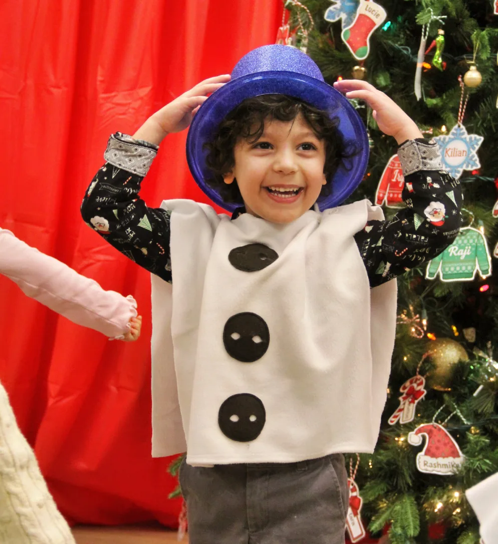 Petit garçon rieur en costume de bonhomme de neige qui tient son chapeau bleu brillant