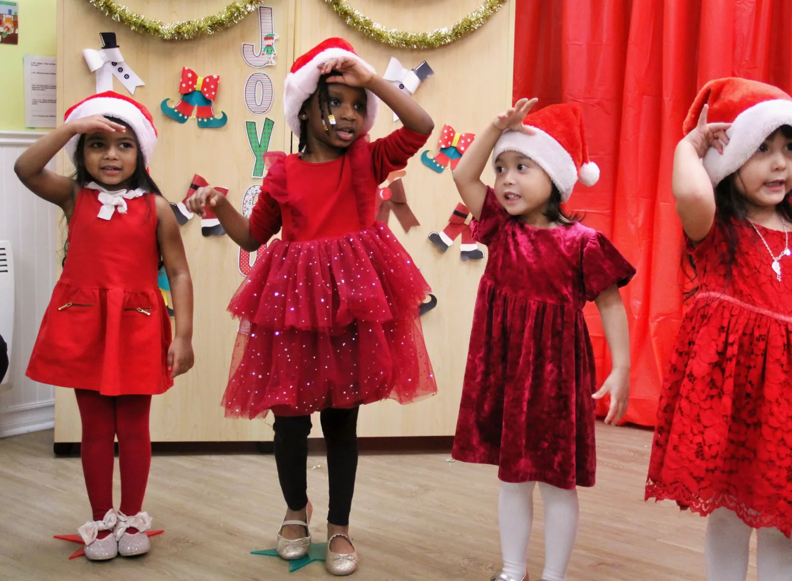 Quatre fillettes en robes rouges et chapeaux de père Noël font des gestes pendant le spectacle