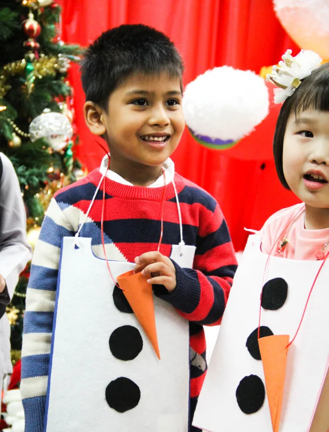 Deux enfants souriants en costumes de bonshommes de neige faits main, avec des nez de carotte en papier