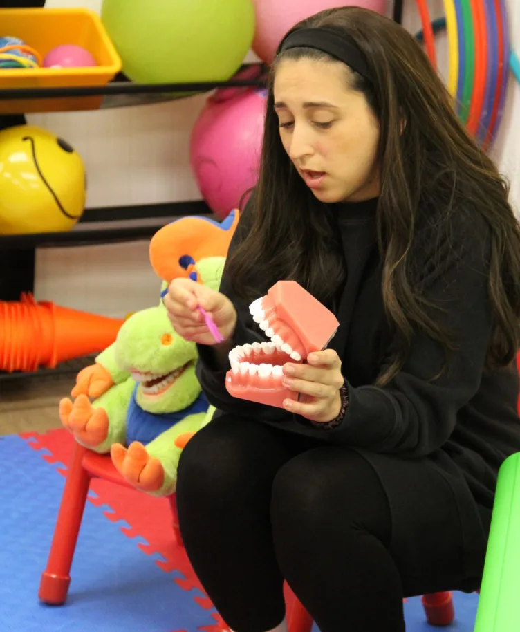 L'hygiéniste montre le brossage des dents sur un modèle géant, le dragon en peluche à ses côtés