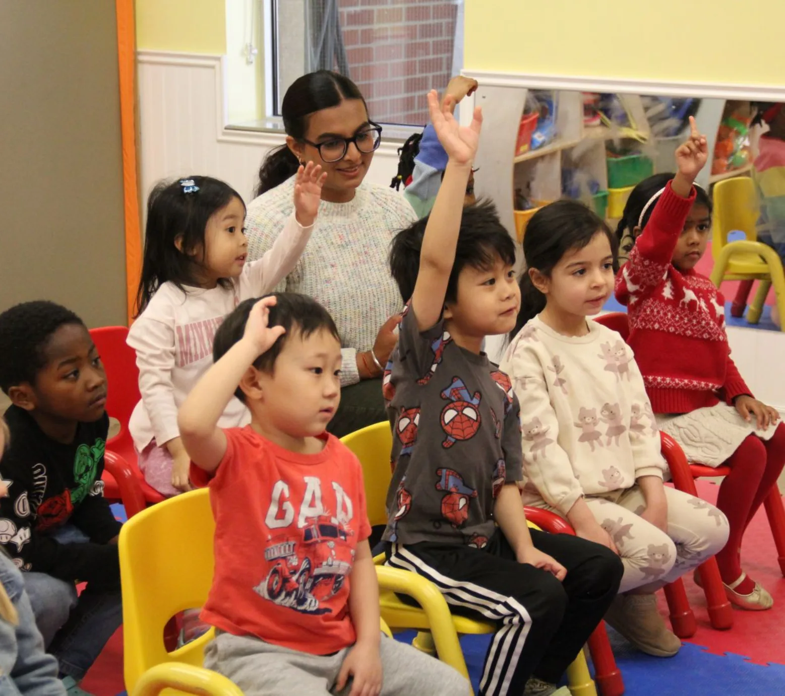 Des tout-petits assis sur de petites chaises lèvent la main avec enthousiasme pendant la présentation
