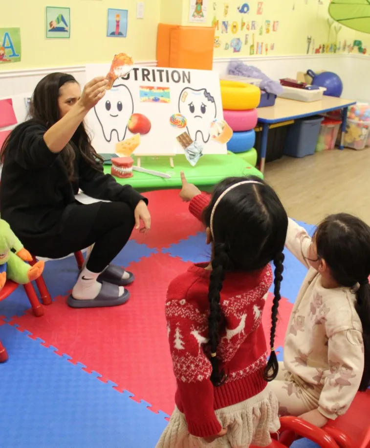 L'hygiéniste pointe une grande dent illustrée sur l'affiche de nutrition devant les enfants attentifs