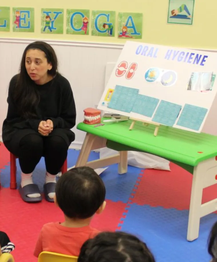 Assise près du tableau sur l'hygiène buccale, l'hygiéniste s'adresse aux enfants installés sur le tapis