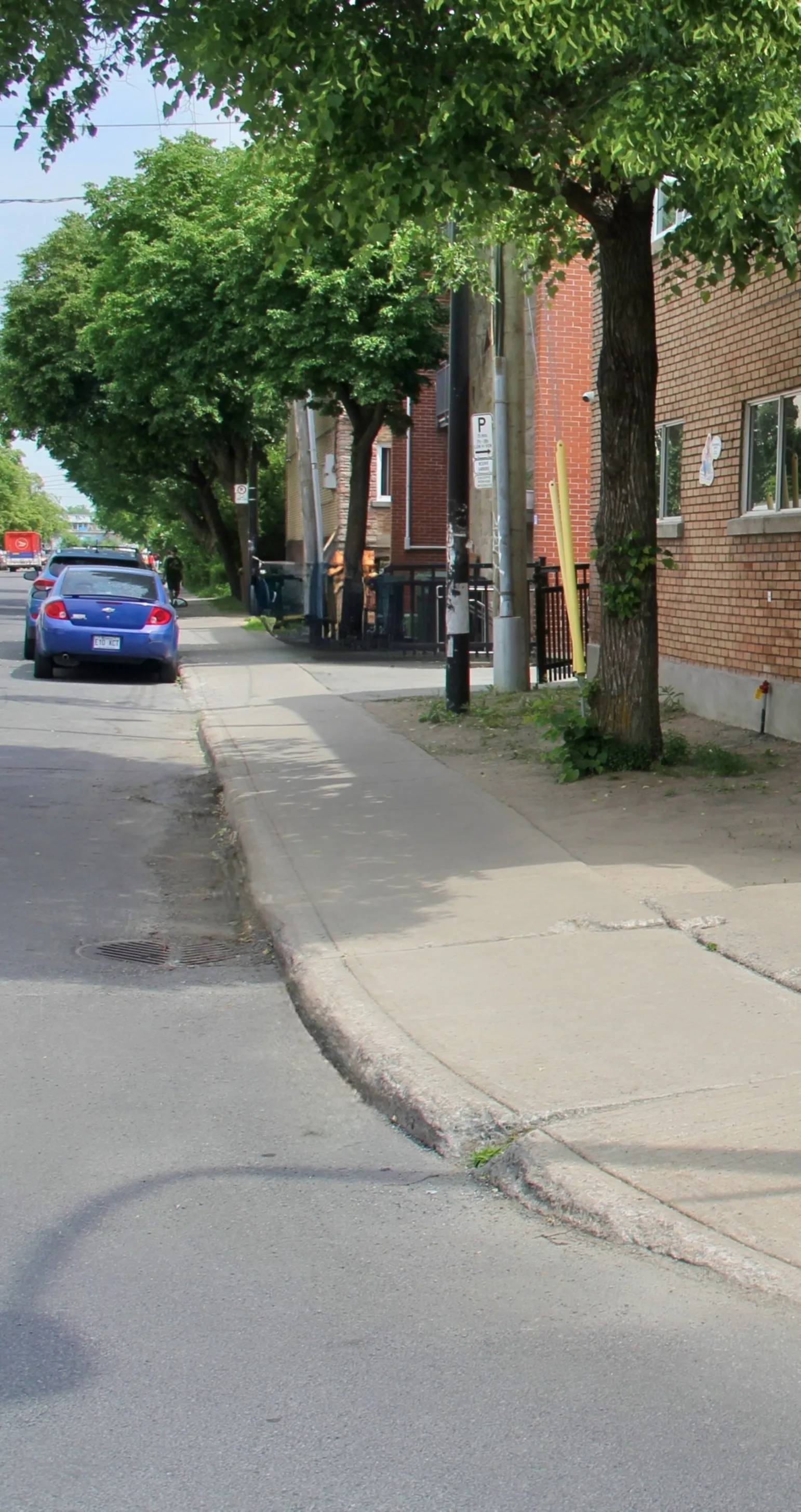 Voiture bleue stationnée dans la rue ombragée, le long du bâtiment en brique de la garderie
