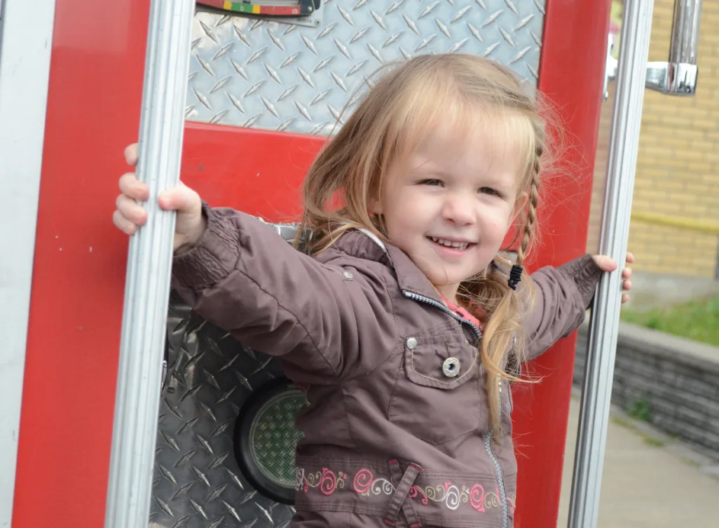 Petite fille souriante agrippée au côté d'un camion de pompiers rouge