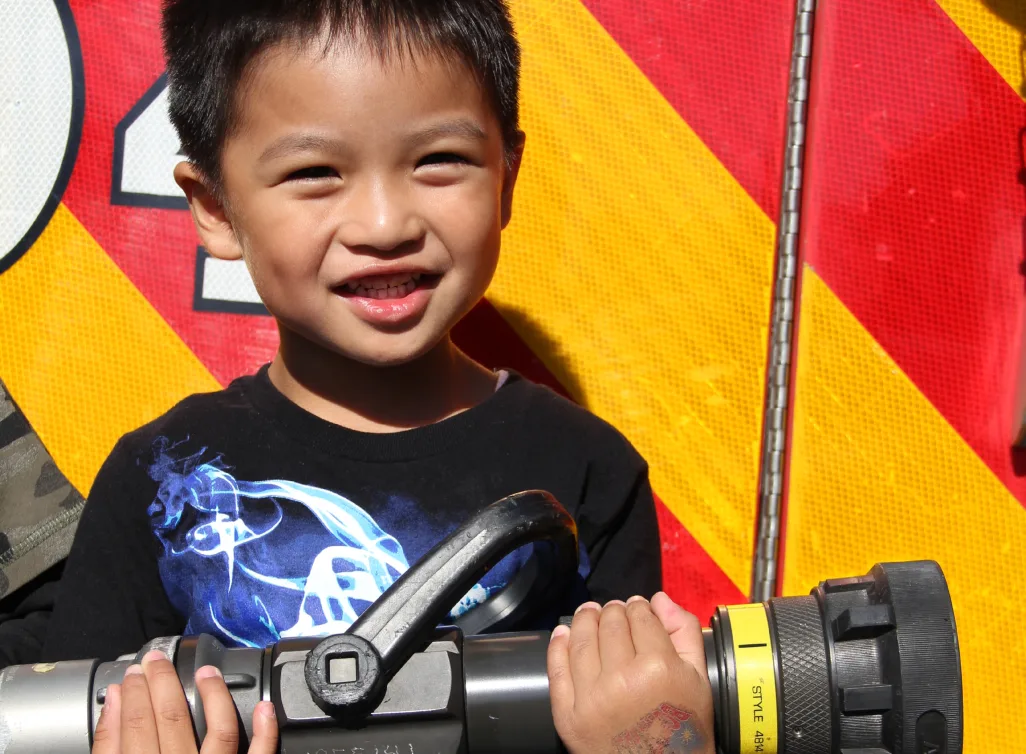 Petit garçon souriant qui tient une lance d'incendie devant le camion de pompiers