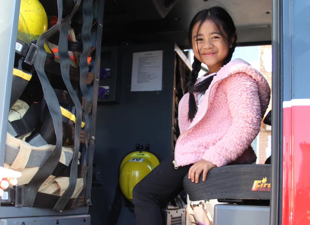 Fillette souriante en chandail rose assise dans la cabine du camion de pompiers