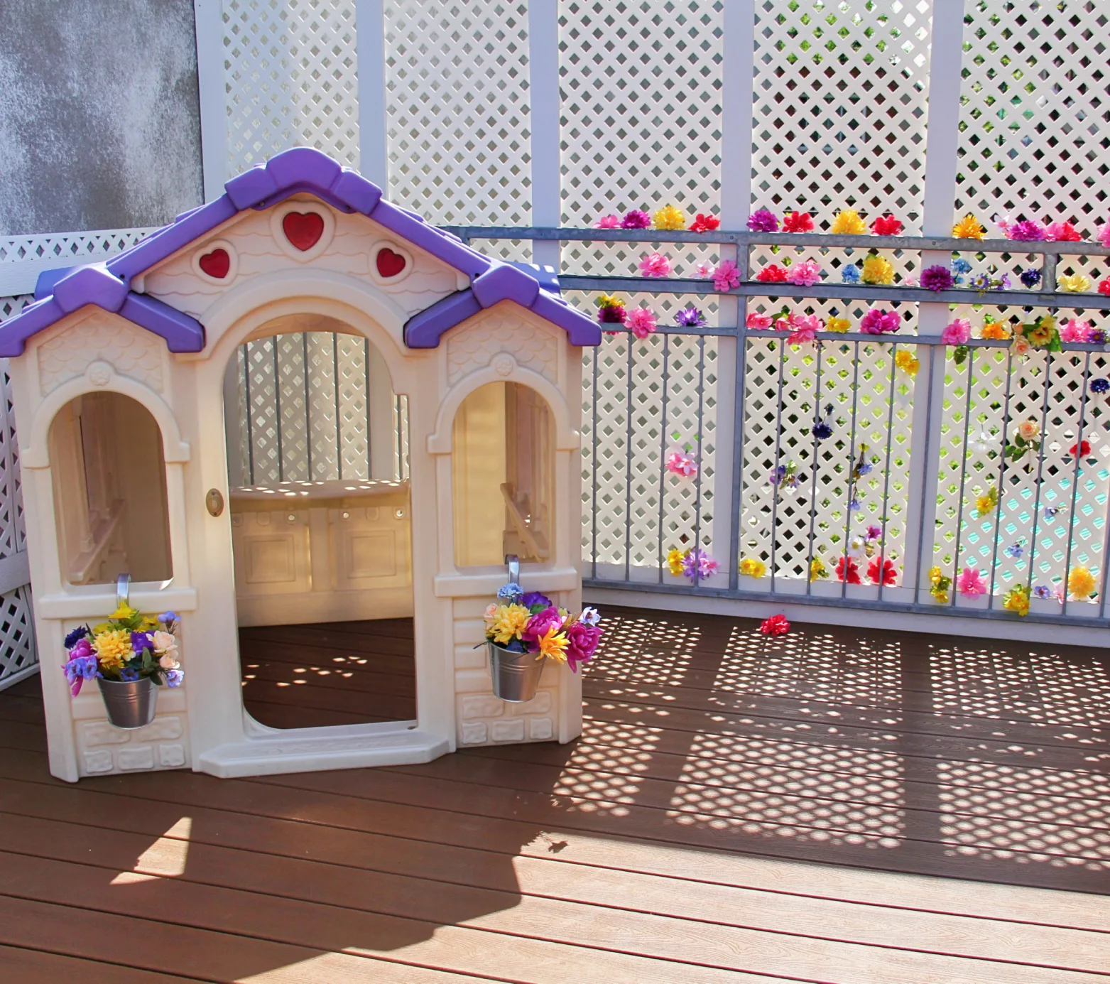 Maisonnette de jeu au toit mauve avec des seaux de fleurs sur la terrasse ensoleillée de la garderie