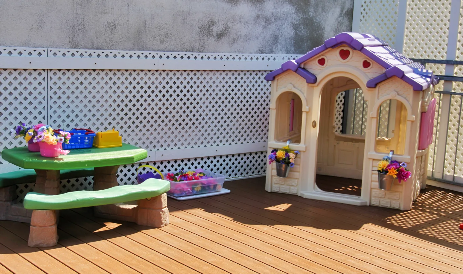 Table à pique-nique verte avec des paniers de fleurs et une maisonnette installées sur la terrasse extérieure
