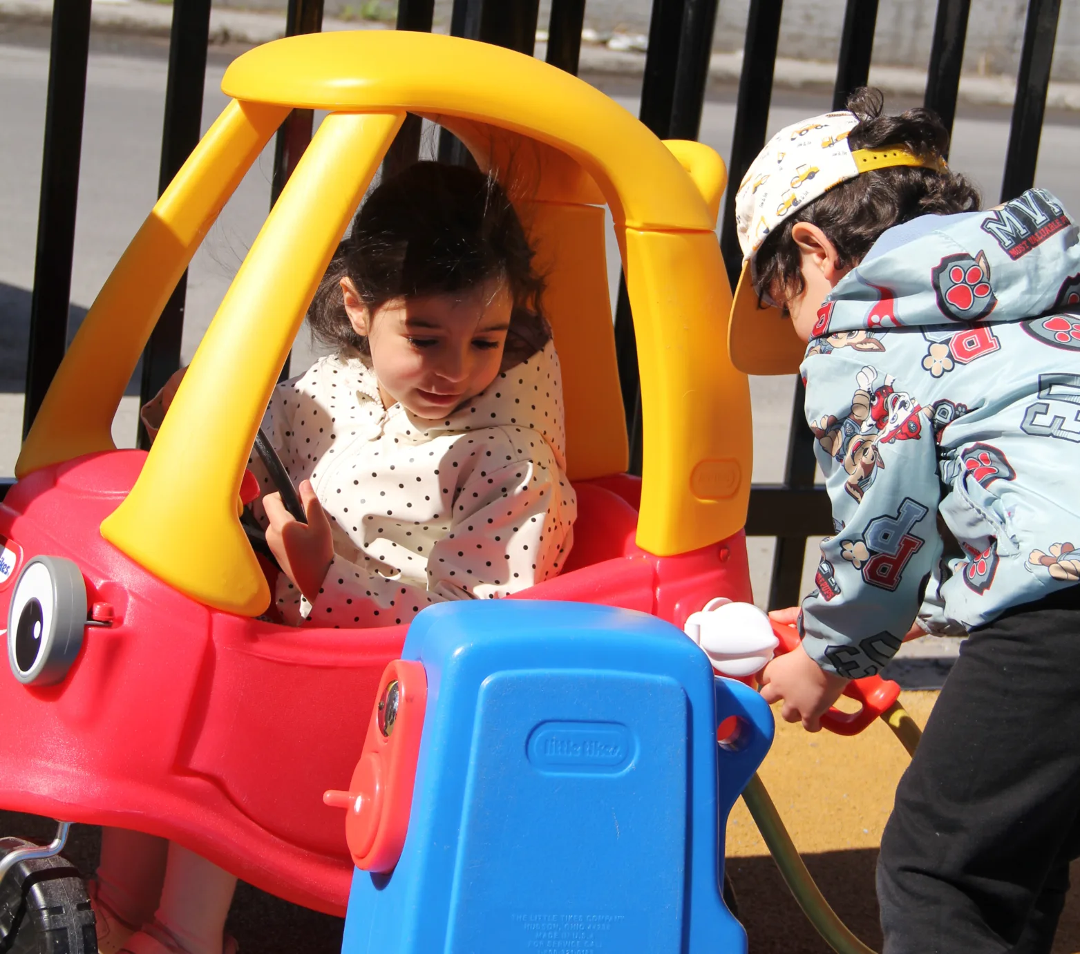 Un enfant fait le plein de la petite voiture pendant que son amie est assise à l'intérieur