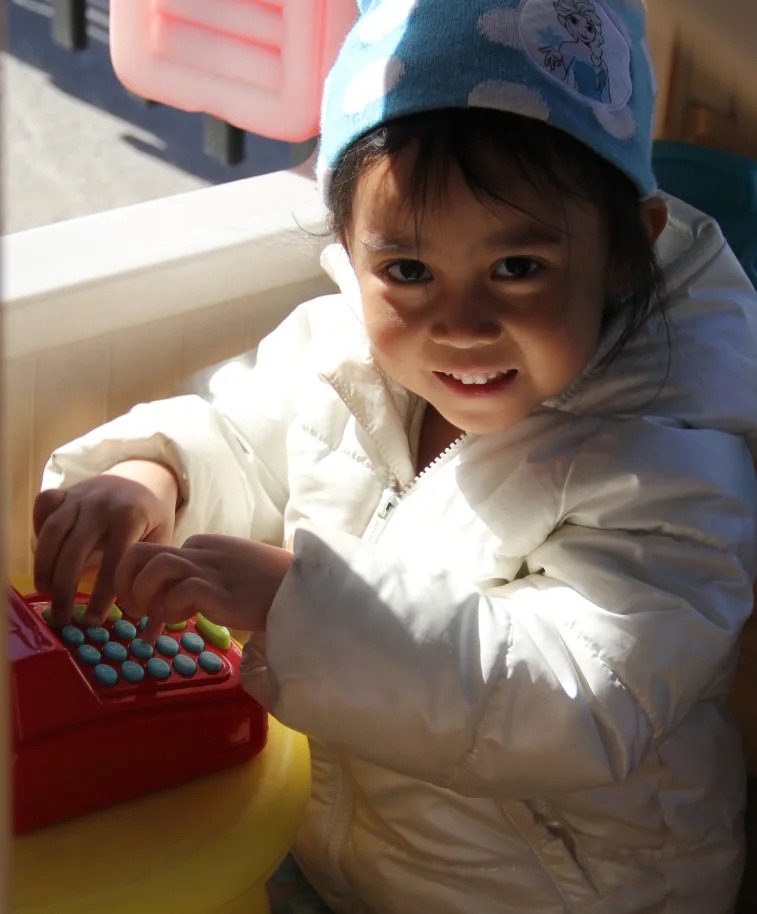 Un tout-petit souriant en manteau blanc pianote sur une caisse enregistreuse jouet rouge