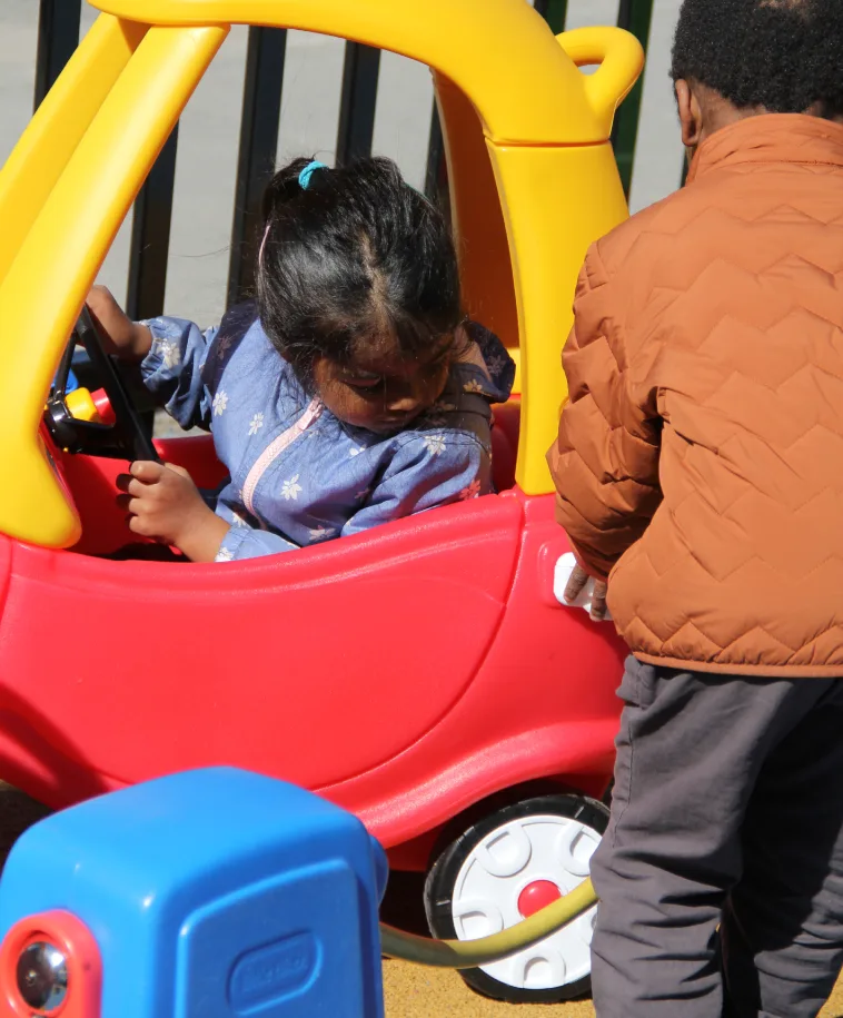 Un enfant se penche dans la petite voiture rouge et jaune près de la pompe à essence jouet