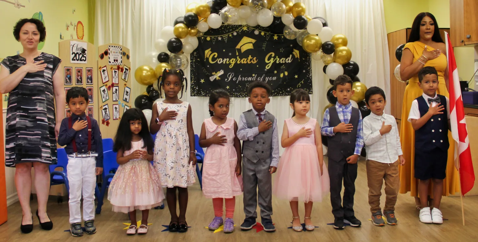 Des enfants en tenue chic, la main sur le cœur, sous une arche de ballons Congrats Grad.