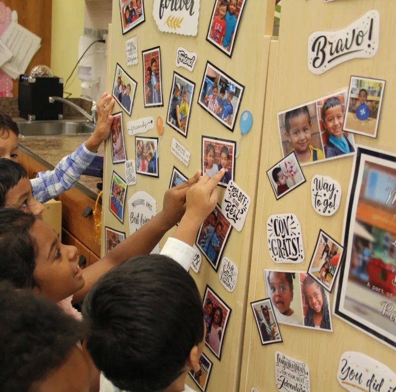 Des enfants pointent un tableau rempli de photos de la classe avec une affiche Bravo.