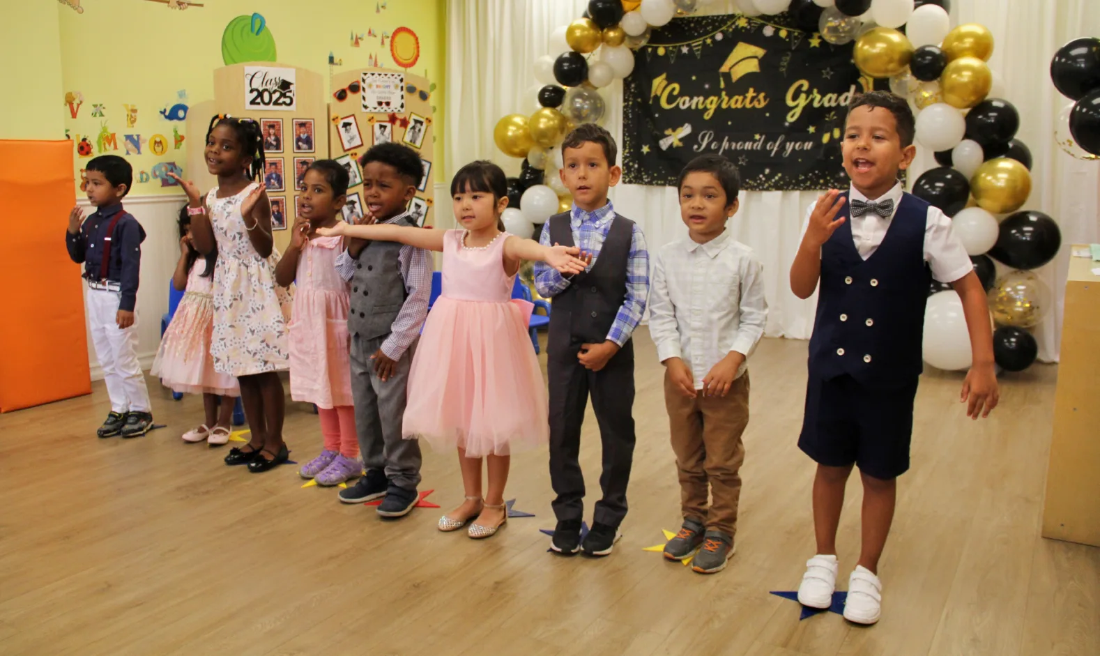 Des enfants chantent ensemble devant une bannière Congrats Grad et des ballons de fête.