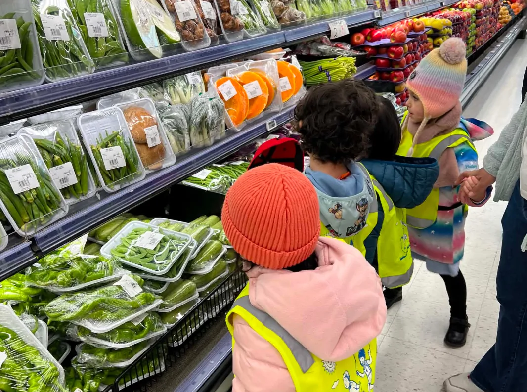 Des enfants en dossards jaunes regardent les légumes frais dans l'allée des fruits et légumes