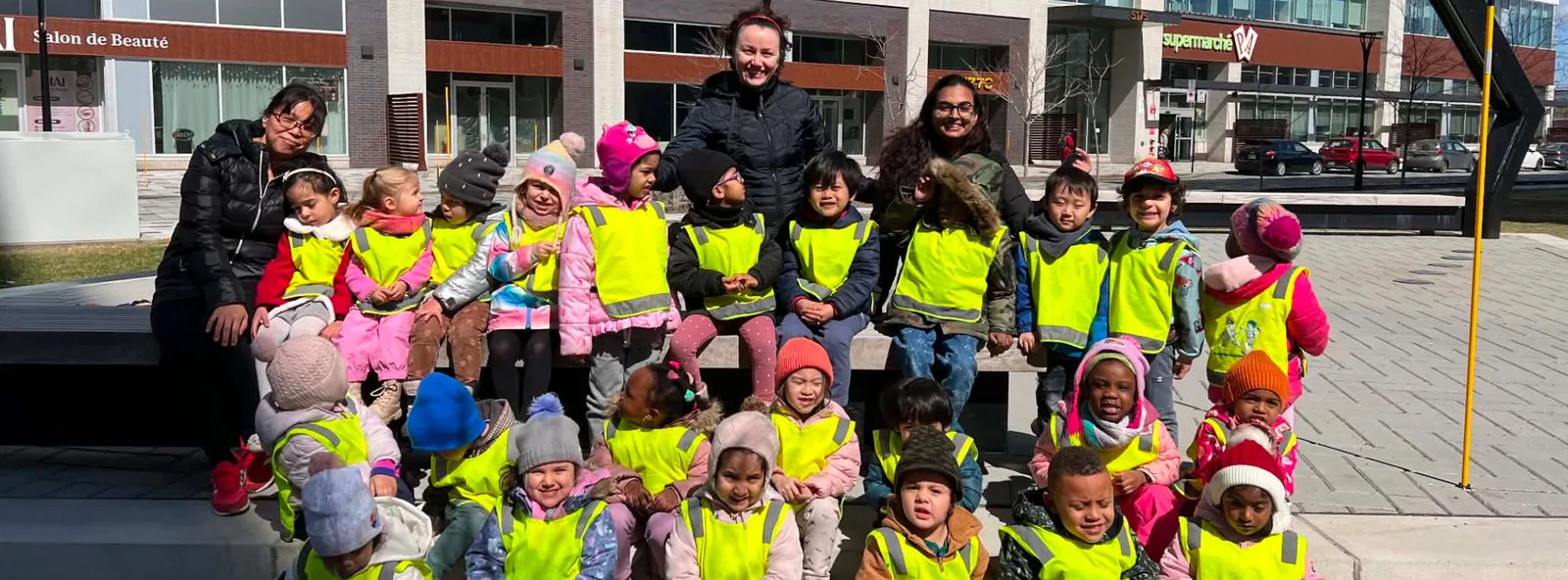 Le groupe de la garderie en dossards jaunes pose avec les éducatrices devant l'épicerie