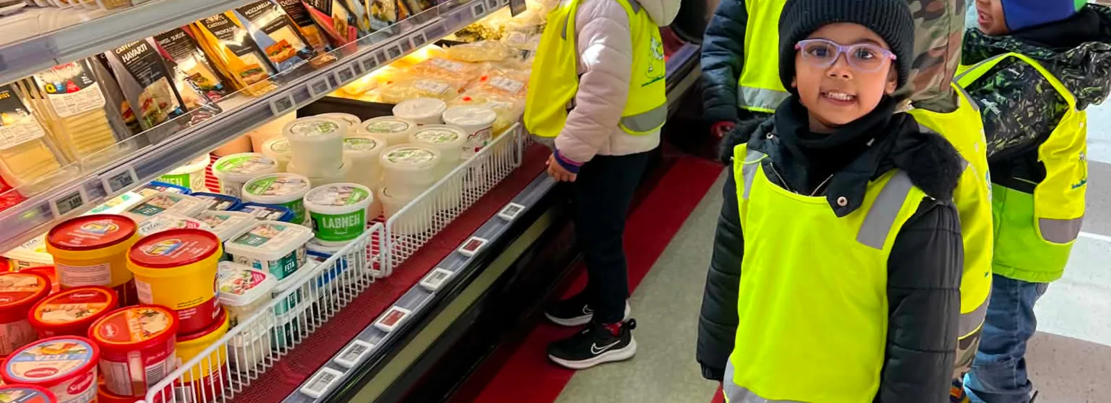 Des enfants en dossards jaunes découvrent la section des produits laitiers à l'épicerie