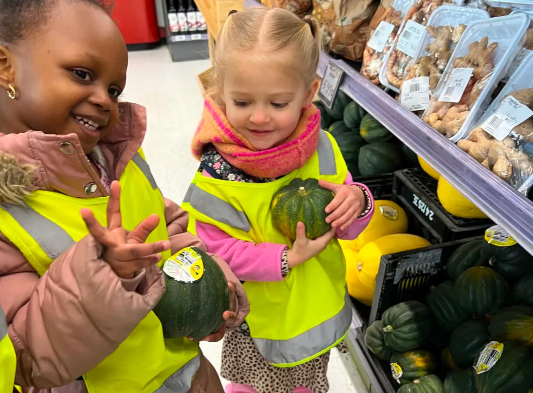 Deux enfants souriants tiennent des courges vertes au rayon des légumes