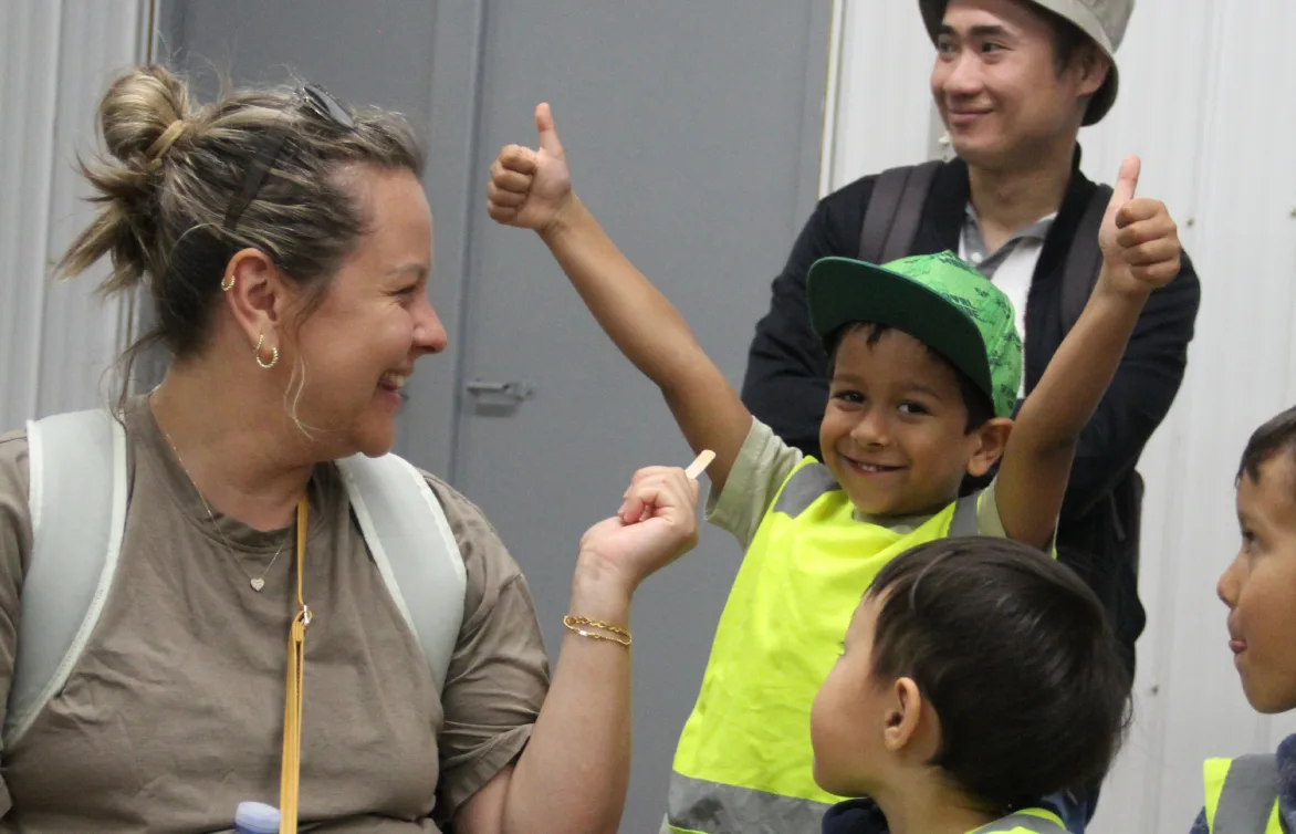 Une adulte souriante discute avec des enfants en dossards qui lèvent le pouce, tout contents