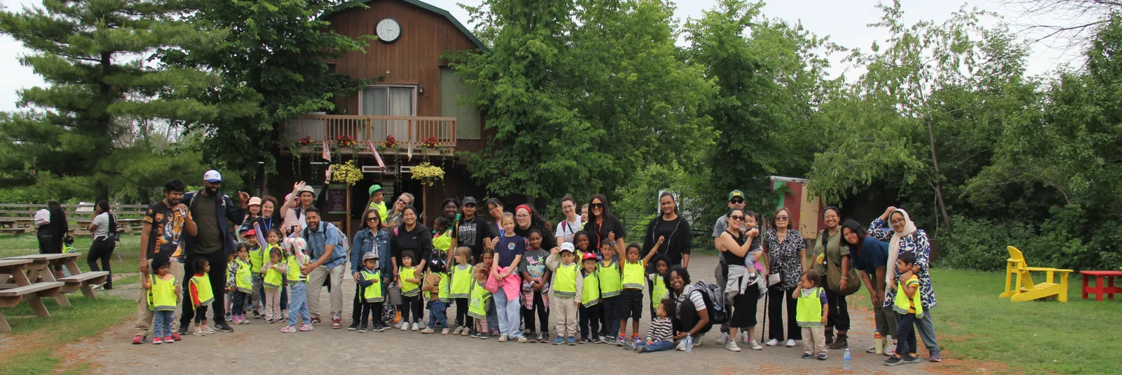 Groupe d'enfants en dossards jaunes avec leurs parents devant un bâtiment de ferme en bois