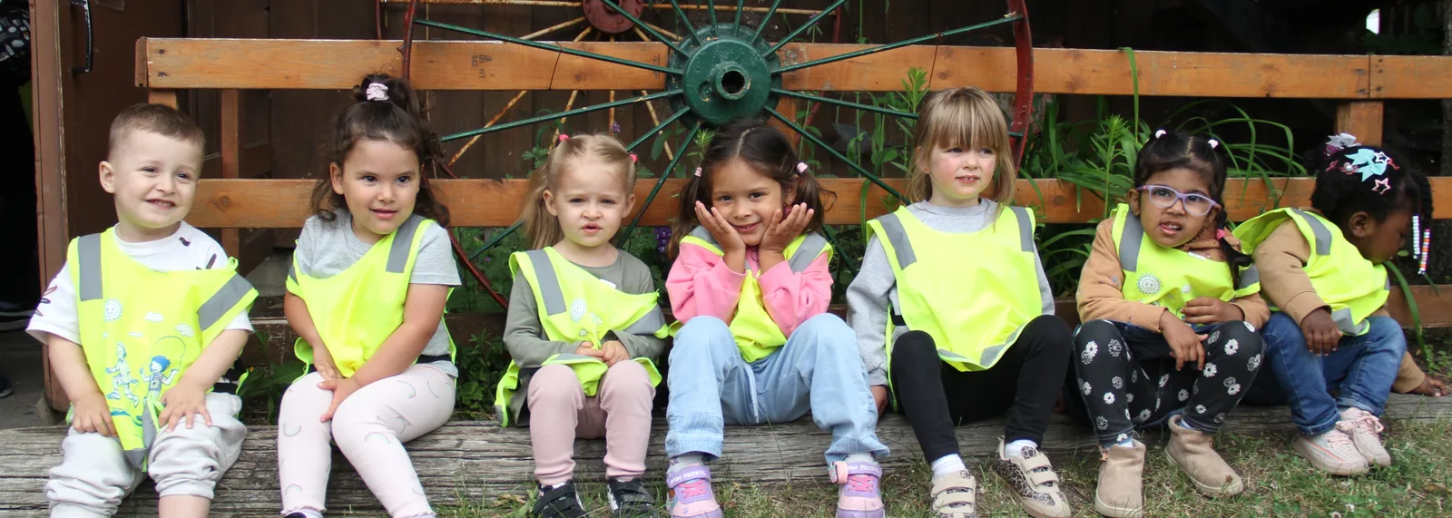 Sept enfants en dossards jaunes assis ensemble devant une vieille roue de charrette