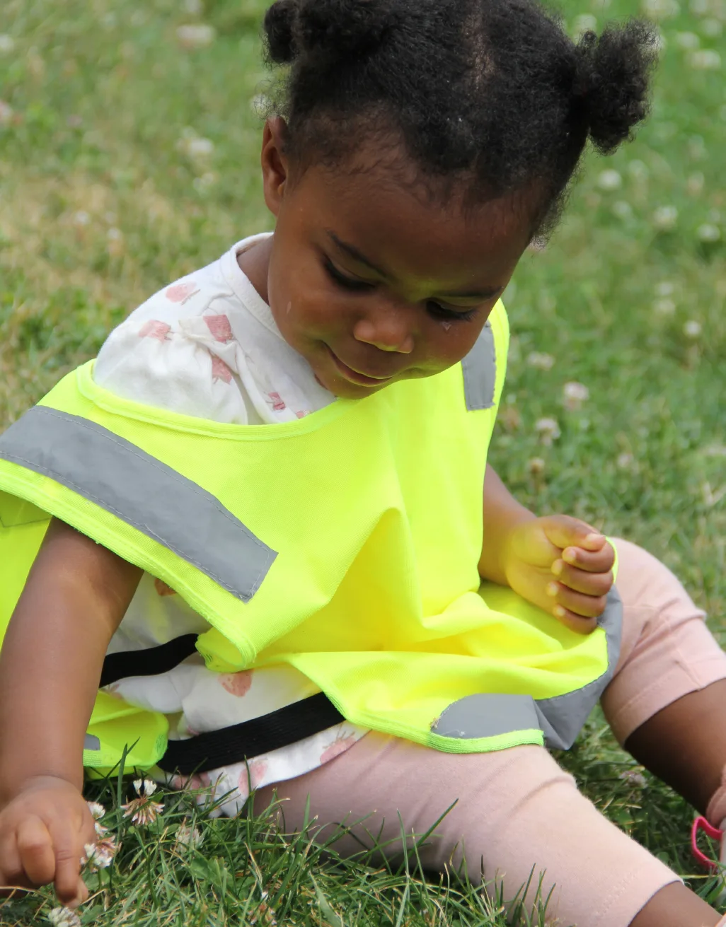 Bambine en dossard jaune assise dans le gazon, le regard vers le sol