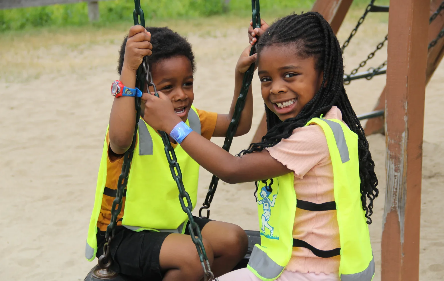 Deux enfants souriants en dossards jaunes assis ensemble sur la balançoire à pneu