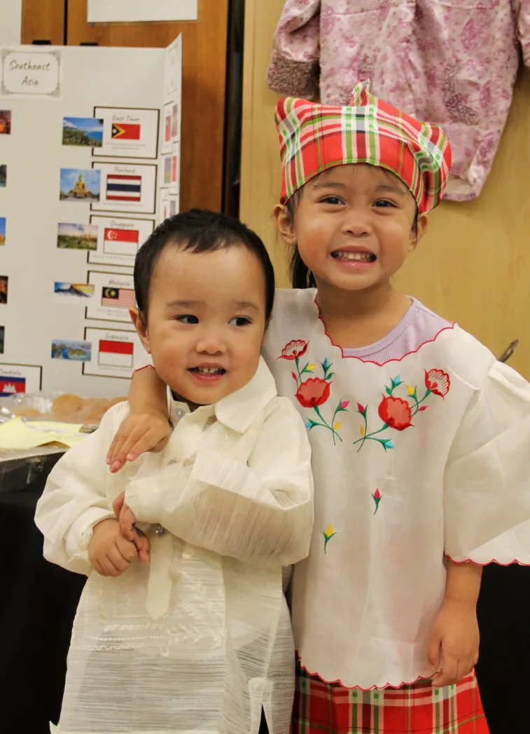 Deux enfants souriants en tenues traditionnelles blanches brodées, dont un avec un foulard à carreaux