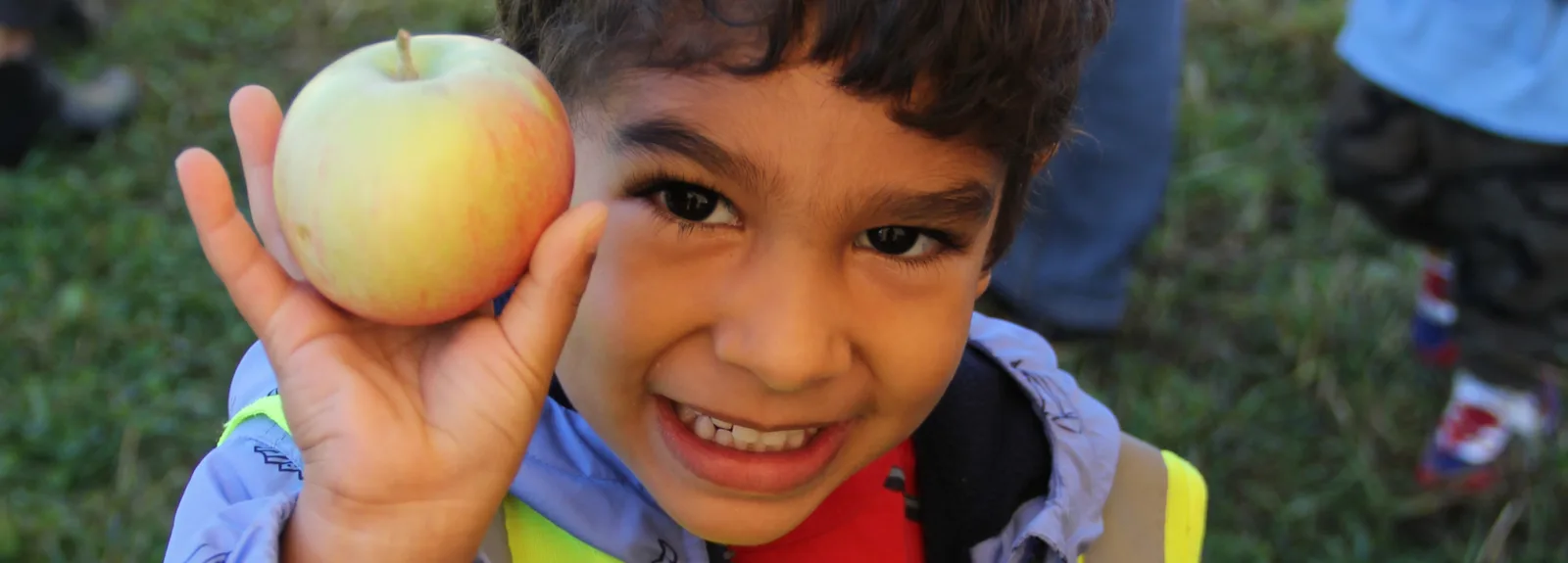Un petit garçon tout souriant montre une belle pomme à côté de son visage