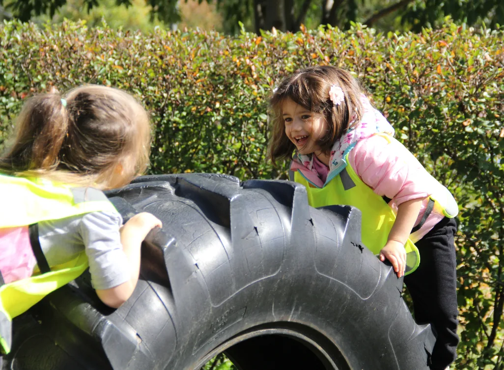 Deux enfants en dossards jaunes s'amusent à grimper sur un gros pneu de tracteur