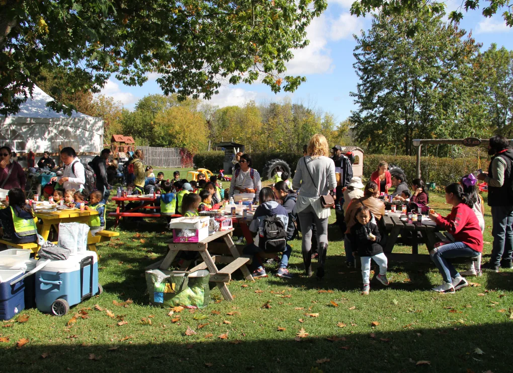 Enfants et adultes pique-niquent ensemble aux tables extérieures sous les arbres d'automne