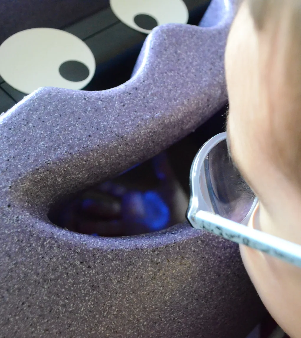 Gros plan d'un enfant avec des lunettes qui regarde dans un appareil d'examen de la vue en mousse mauve
