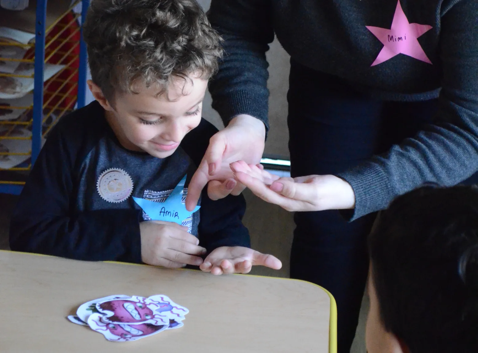 Un petit garçon aux cheveux bouclés observe attentivement une infirmière qui fait une démonstration avec ses mains