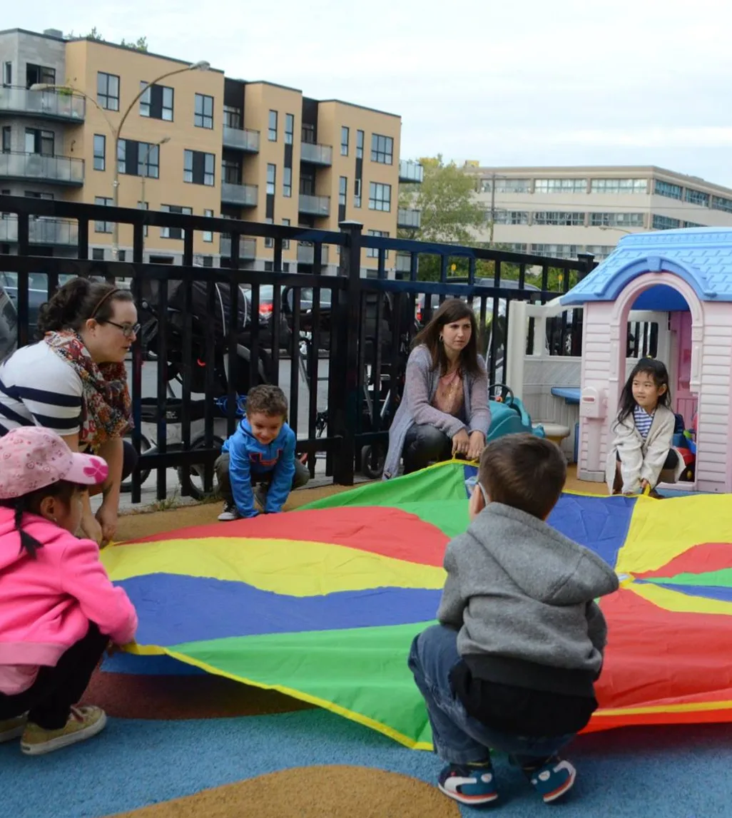 Des enfants rassemblés autour d'un parachute multicolore dans la cour clôturée de la garderie