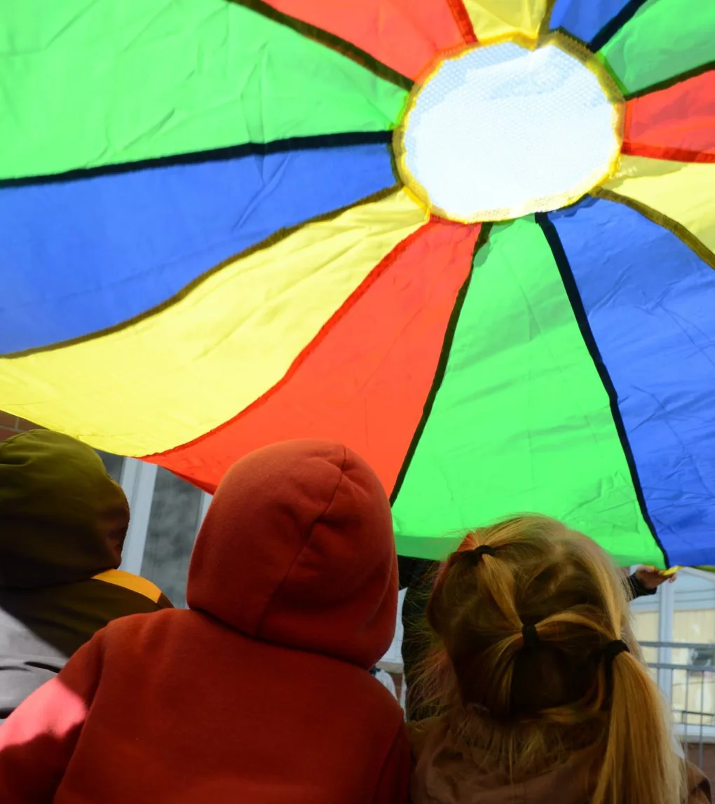 Deux enfants vus de dos regardent le parachute arc-en-ciel soulevé au-dessus d'eux