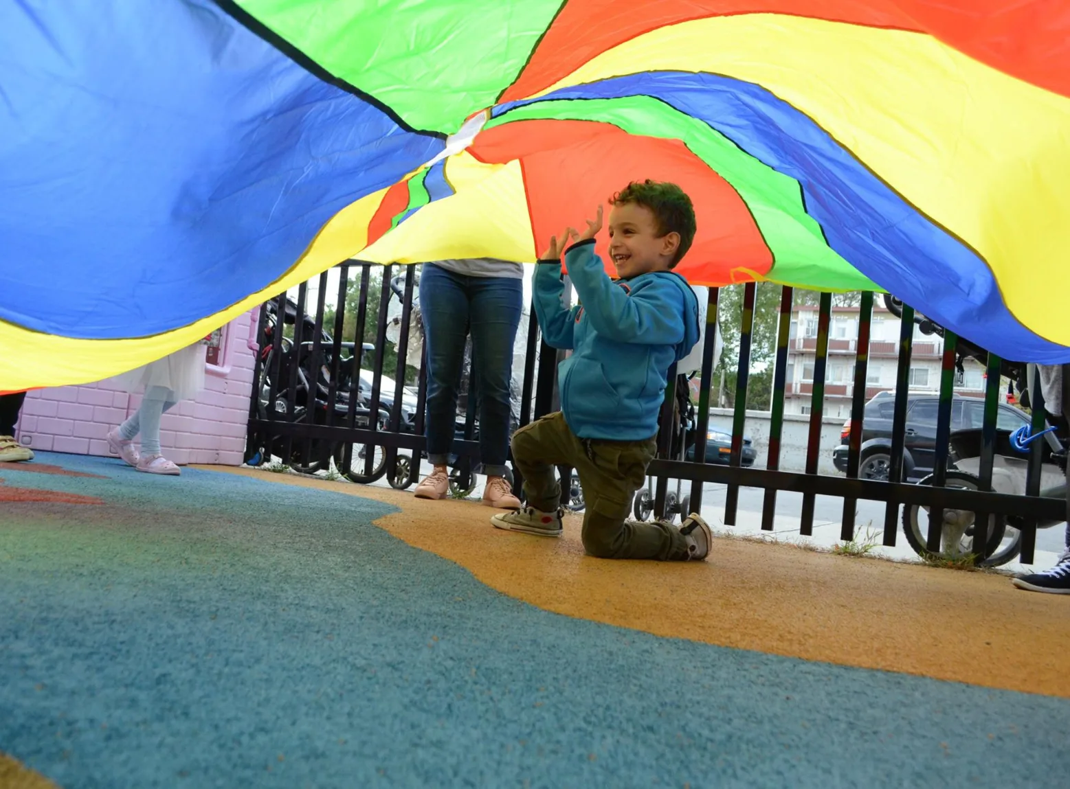 Un garçon souriant à genoux sous le parachute, sur le sol souple de la cour extérieure